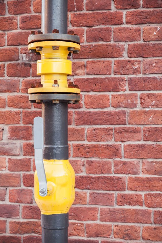 Gas tubing with open valve above red brick wall