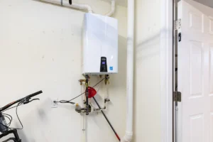Wall-mounted tankless water heater installed in a garage with visible plumbing and venting connections. Best for blogs about tankless water heaters, water heater installation, hot water systems, and residential plumbing equipment.