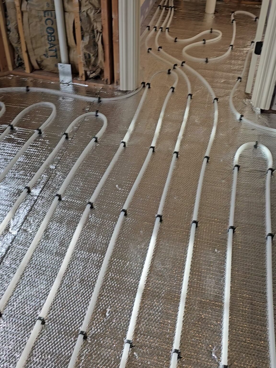 Radiant heating tubing layout: loops clipped over reflective insulation on a subfloor, installed by Absolute Precision