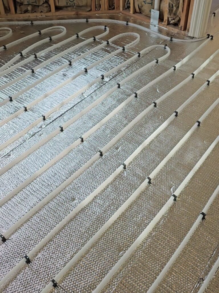 Radiant heating tubing clipped over foil insulation across a room floor before the finish floor goes down
