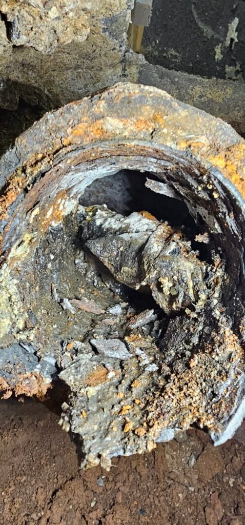 Cross-section of an old drain pipe with flaking rust and debris, the kind of buildup a sewer camera inspection can find